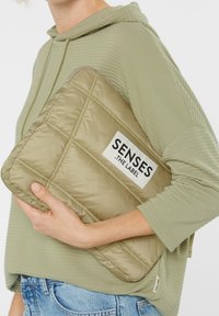 Gepolsterte Laptoptasche in einem sanften Olivgrün, gefertigt aus glattem Nylon. Verfügt über ein auffälliges Logo-Patch in Schwarz und Weiß sowie dezent gehaltene Nähte.