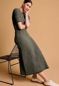 Robe en tricot gris à manches courtes, silhouette évasée et tissu texturé. Associée à des baskets beiges et un collier en chaîne dorée.