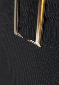 Tissu noir côtelé avec un fermoir rectangulaire doré brillant, présentant une surface texturée et des coutures invisibles le long du bord.