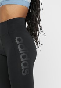 Närbild av en person som bär svarta Adidas-tights med hög midja och en ljusblå sportbh, med långt flätat hår.