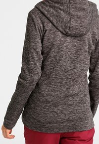 Szary, fakturowany hoodie z kapturem, widocznymi detalami szwów i dopasowanym krojem. Rękawy sięgają nadgarstków, noszony na burgundowych spodniach.