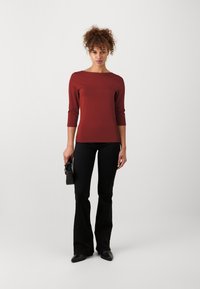 Maroon fitted long-sleeve shirt with boat neckline, paired with black flared trousers and black handbag, set against a light background.