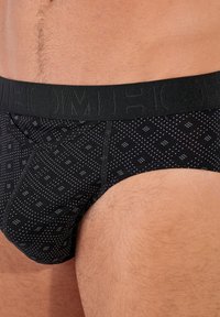 Schwarze Baumwollunterwäsche mit einem gemusterten Design, das kleine blaue Quadrate zeigt. Der Bund ist elastisch und mit dem Markennamen geprägt.