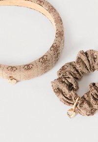 Σετ αξεσουάρ μαλλιών που περιλαμβάνει ένα παχύ πλεκτό καφέ στεφάνι με λουλουδάτο μοτίβο και ένα ταίριαστο scrunchie με ένα μενταγιόν σε σχήμα καρδιάς.