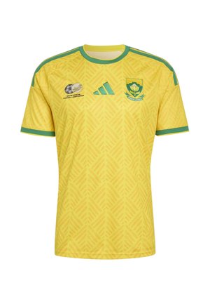 Κίτρινη φανέλα ποδοσφαίρου της Νότιας Αφρικής με πράσινο τελείωμα, υφασμάτινο μοτίβο, λογότυπα της Νοτιοαφρικανικής Ποδοσφαιρικής Ομοσπονδίας και της Adidas, και έμβλημα της ομάδας στο στήθος.