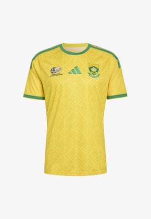 Tricou galben de fotbal sud-african cu margini verzi, material cu model, siglele Asociației de Fotbal din Africa de Sud și Adidas, și emblema echipei pe piept.