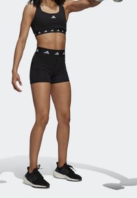 Musta urheil bra ja shortsikoko, joissa on valkoiset Adidas-logo-yksityiskohdat. Tyylikäs muotoilu, tiukka malli ja kontrastivärinen pohja mustissa lenkkareissa.