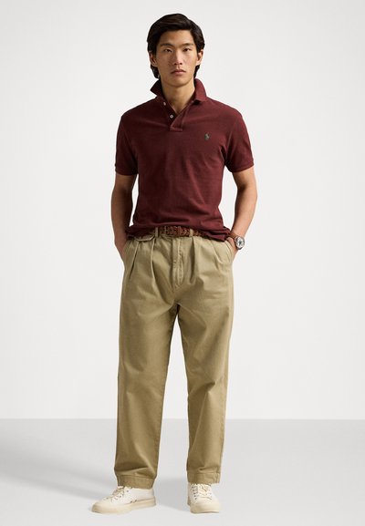 Tricou polo bordô cu guler, asortat cu pantaloni bej plisat și adidași crem. Prezintă un mic logo verde pe piept.