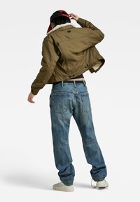 Khaki jasje met een nepbont kraag, ritssluiting aan de achterkant en knopen; gecombineerd met lichtblauwe jeans met een relaxed fit en subtiele stiksels.