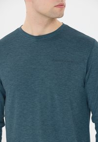 Herren Langarmhemd in Teal, aus strukturiertem Stoff. Mit Rundhalsausschnitt und dezentem "ENDURANCE"-Logo in Schwarz.