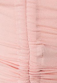 Růžová elastická tkanina se stočenou texturou, která ukazuje švy a elastické vlastnosti. Detailní pohled zdůrazňuje vodorovné sklady.