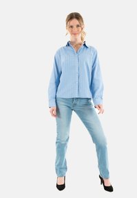 Camicia a righe blu chiaro, taglio rilassato; abbinata a jeans in denim chiaro e tacchi neri alti. Tessuto morbido e design del colletto classico.