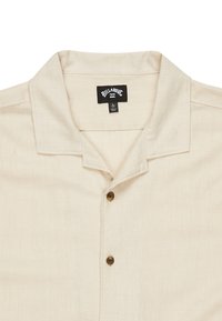 Beige kortærmet skjorte lavet af hør, med en camp krave og tre brune knapper ned ad fronten. Etiket synlig ved halsudskæringen.