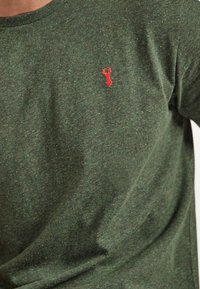 Grøn kortærmet t-shirt lavet af tekstureret stof, med et lille rødt hummer emblem på brystet. Blødt og afslappet design.