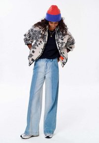 Textúrovaná bielo-čierna fleecová bunda, modré tričko, široké svetlomodré džínsy, farebná pletená čiapka a sivé tenisky.