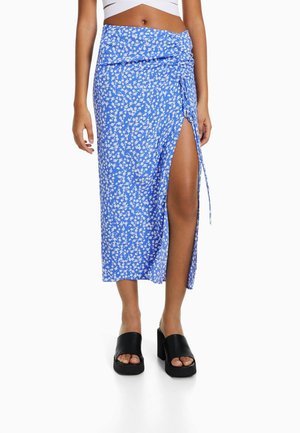 Blå blommig midi-kjol med hög sidoklyvning. Lättviktsmaterial med en knytning vid midjan. Bärs med kraftiga svarta platåsandaler.