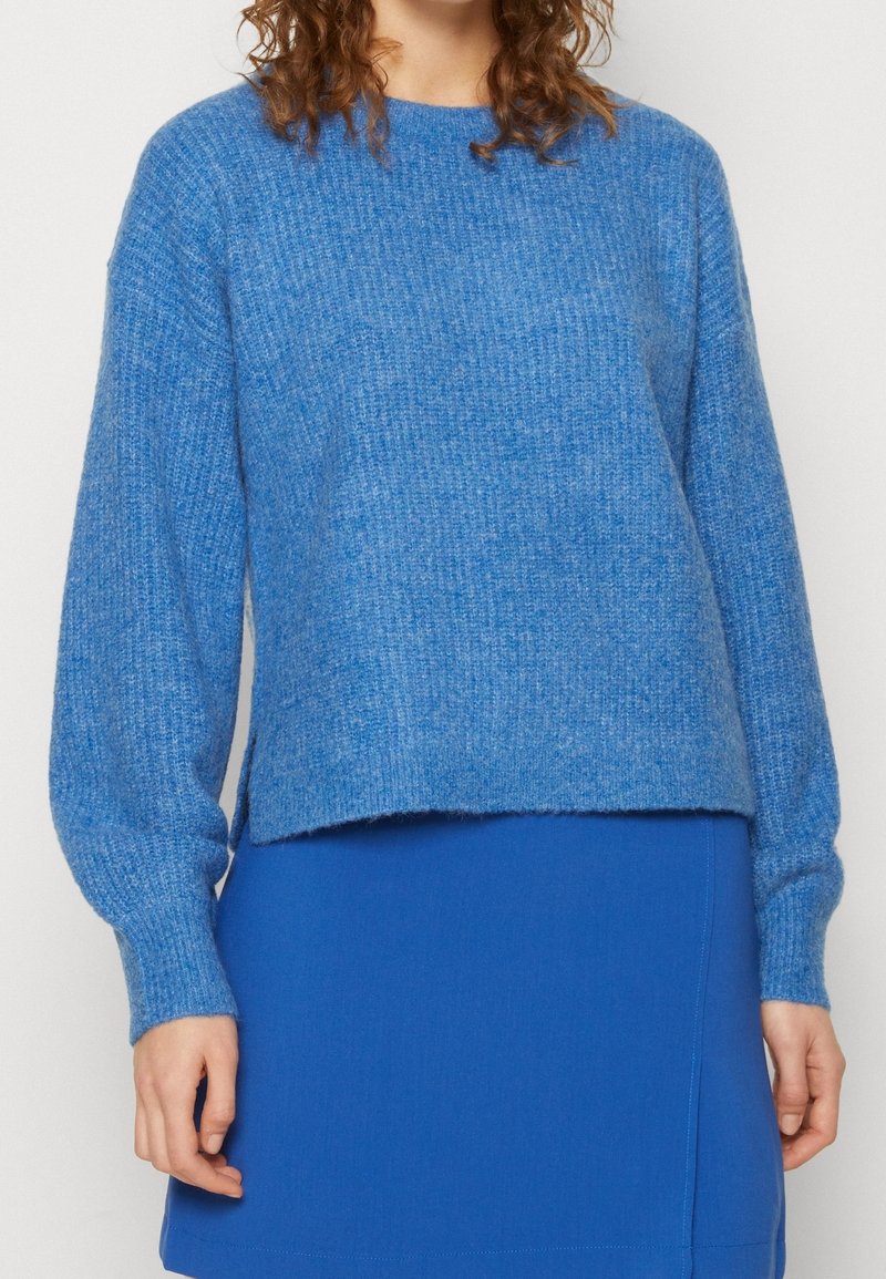 Blauer Strickpullover mit langen Ärmeln, Rundhalsausschnitt und leicht verkürztem Saum. Der Stoff zeigt eine weiche Textur in einheitlicher Farbe.