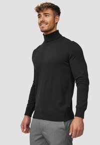 Suéter negro de cuello alto, hecho de material suave, con un diseño ajustado, cuello y puños acanalados, y con aberturas laterales en el dobladillo para mayor libertad de movimiento.