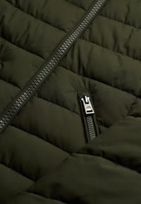 Chaqueta aislante verde oscuro con patrón acolchado, que presenta una cremallera central y tirador metálico, fabricada con un tejido liso y ligero.