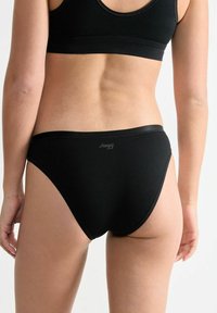 Schwarze Baumwollunterwäsche mit glattem Stoff, hohe Beinaschlaufen und minimalistischer Markenlogos am Bund. Einfach und funktional.