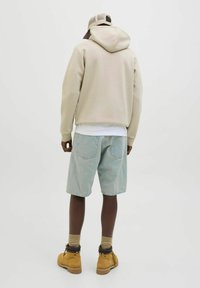 Beige Kapuzenpullover mit Kapuze, hellblaue Denim-Shorts, beige Stiefel und eine Mütze. Der Stoff wirkt weich, hat eine lockere Passform und sichtbare Taschen.