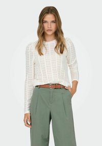 Light cream lace top with long sleeves and puffed shoulders, paired with olive green wide-leg trousers and a brown belt.