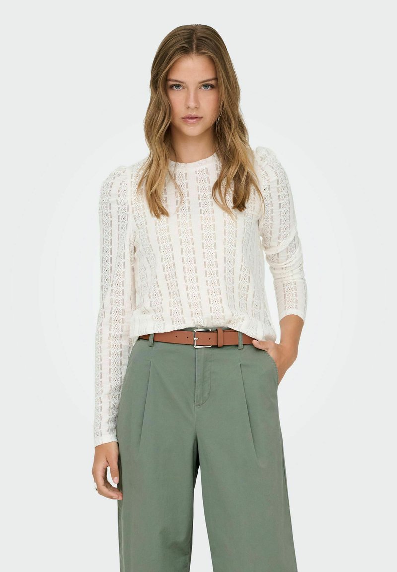 Light cream lace top with long sleeves and puffed shoulders, paired with olive green wide-leg trousers and a brown belt.
