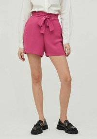 Fuchsiové šortky s elastickým pasem a mašlí, s hladkým povrchem a volným střihem, doplněné černými mokasíny.
