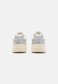 Vue arrière de baskets beiges et argentées avec un dessus en mesh texturé, un col rembourré et un détail de logo contrastant sur le talon.