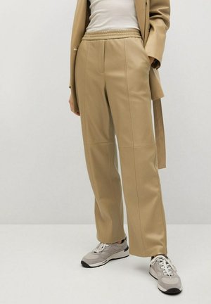 Beige, wijde broek van glad stof, met een trekkoord in de taille en verticale naden, gecombineerd met grijze sneakers.