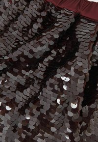 Fényes, textúrált felülettel rendelkező, sötét bordó színű, egymásra fedett kör alakú flitterekkel díszített flitter szoknya, begyűrt, rugalmas derékpánttal.