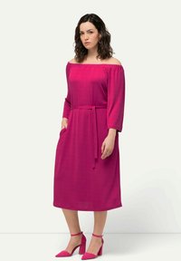 Fuchsia off-shoulder mekko, jossa on kolmanneksen hihat, vyötä ympärillä ja sivutaskut; pehmeä kangas, jonka pinta on sileä. Yhteensopivat vaaleanpunaiset korkokengät.