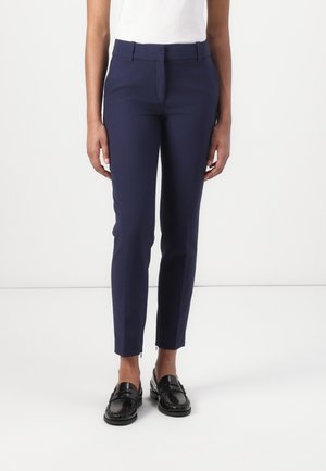 Navy blue fitted trousers with a smooth texture, tapered legs, zip accents at the hem, and a flat front design. Paired with black shoes.