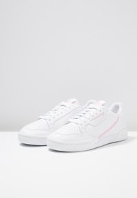 Sneaker sportive bianche con tomaia in pelle testurizzata, dettagli rosa, perforazioni decorative e suola piatta in gomma con logo.