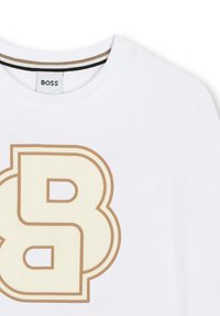 T-shirt BOSS blanc avec un grand logo double-B stylisé beige et marron sur la poitrine et une bordure rayée le long du col.