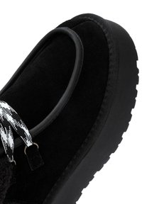 Czarne zamszowe buty z grubą gumową podeszwą, z tekstylnym paskiem w zygzakowaty wzór i zaokrąglonym obcasem dla dodatkowego wsparcia.