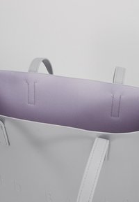 Szara torba tote o gładkiej fakturze, z lawendowym wnętrzem. Emituje czyste linie i minimalistyczny design, z płaskimi ramiączkami i subtelnym brandowaniem.