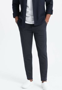 Pantaloni navy a trama con vestibilità slim, dotati di tasche laterali. Abbinate a una maglietta bianca e scarpe slip-on bianche.