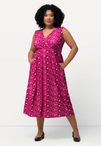 Vaaleanpunainen mekko, jossa on kietaisumalli, hihaton leikkaus ja taskut. Musta-valkoisilla muodoilla kuvioitu, ulottuu polven keskelle. Yhdistetty mustiin kenkiin.