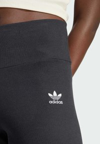 Mørkegrå ribbede leggings med bred midjebånd og hvit Adidas-logo nederst til venstre. Myk, elastisk stoff for komfort.