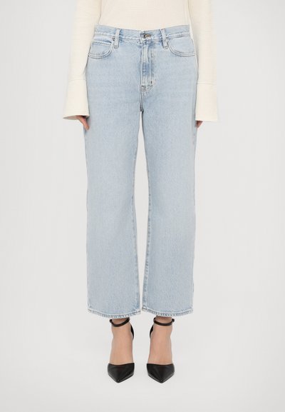 Blugi largi din denim de culoare bleu deschis, cu talie înaltă, margini țesute și design cu cinci buzunare, purtați împreună cu tocuri negre cu vârful ascuțit.