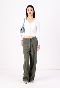 Haut court à manches longues blanc côtelé, pantalon vert olive ample avec taille à cordon de serrage, baskets argentées et petit sac à bandoulière bleu.