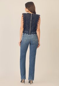 Top in pizzo blu navy con maniche a scallop, chiusura con zip sul retro. Abbinato a jeans dritti azzurri e tacchi alti neri.