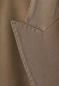 Beige stof met een gladde textuur, gekenmerkt door een scherpe kraagrand en zichtbare stikseldetails, die een op maat gemaakte ontwerpen laat zien.