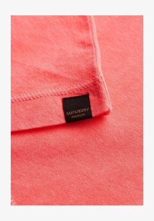 Koraalkleurig katoenen T-shirt met een gladde textuur, voorzien van een zwart label met de tekst "SUPERDRY PREMIUM" op de hals.