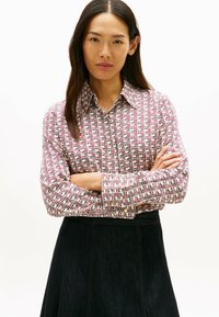 Camisa de cuadros en blanco, rojo y azul. Cuenta con mangas largas y un cuello clásico, combinada con una falda oscura.