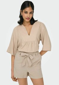 Beige Leinenoberteil mit V-Ausschnitt und Raffung, kombiniert mit passenden hoch taillierten Shorts mit Bindegürtel und seitlichen Taschen.