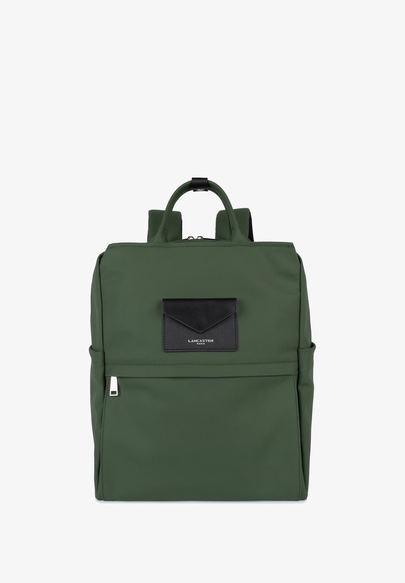 Sac à dos en nylon vert avec des accents en cuir noir, comportant une poche avant, des poignées supérieures doubles et des bretelles rembourrées. Texture lisse.