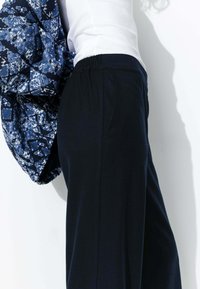Pantalons larges noirs avec taille élastique associés à une veste en jean bleu matelassée à motifs, mettant en valeur un tissu texturé et une coupe loose.