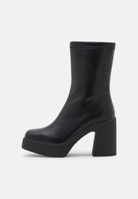Bottes cheville noires en cuir lisse, plateforme noire texturée et épaisse, talon bloc haut. Design minimaliste sans accents supplémentaires.